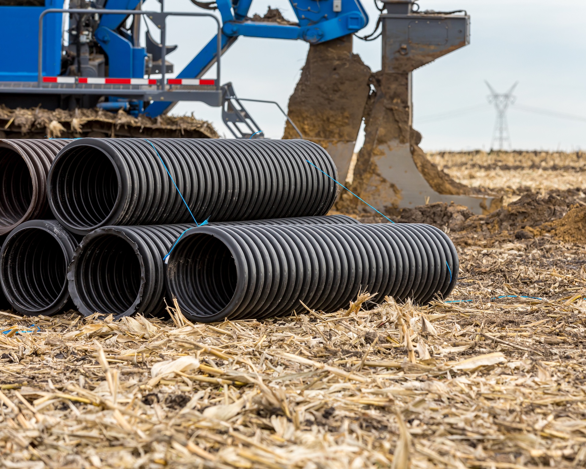 Black corrugated water drainage pipe, field tile, in farm field with tile plow or ditcher in background